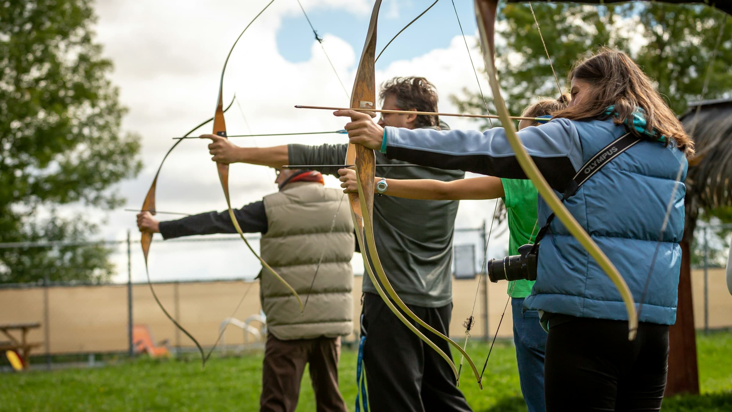 A group of archers practicing with traditional longbows on an outdoor range